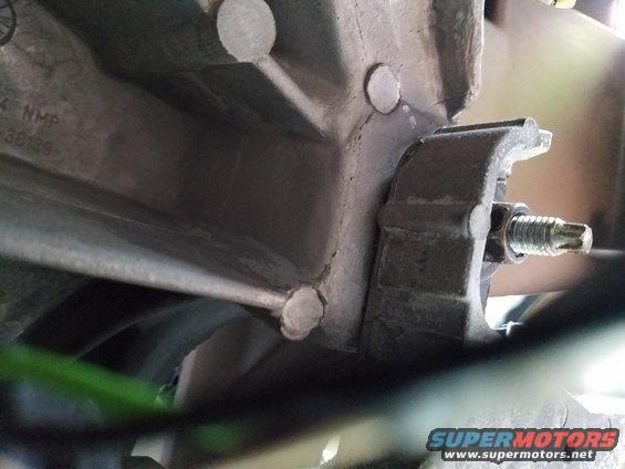 Close-up of a metal bracket with a bolt attached to a larger metal component, with some green material visible below