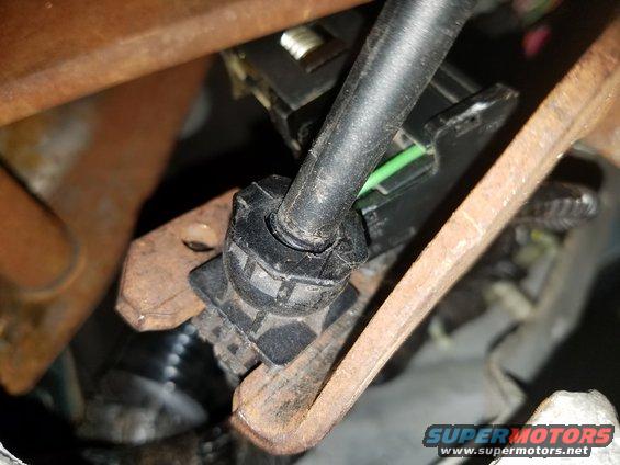 Close-up of a black plastic connector with a black cable and green wire attached, mounted on rusty metal brackets