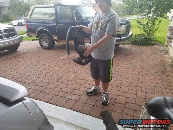 Guy holding dashboard piece in front of blue Ford Bronco