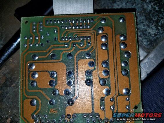 Close-up of a green circuit board with copper traces and solder points. A small Ford logo is visible