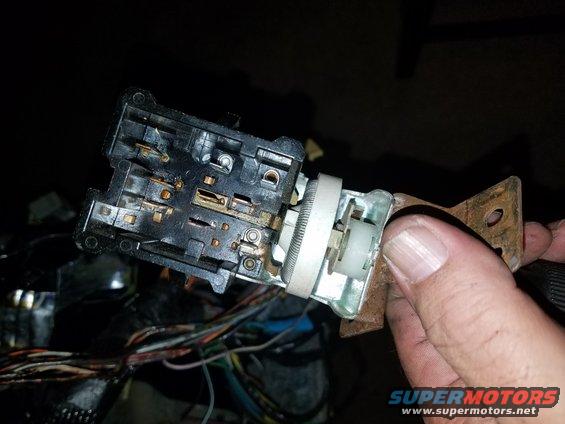 Headlight switch assembly with wires and mounting bracket. Hand holding the part
