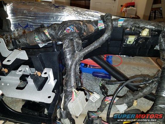 Vehicle wiring harness with black tape and connectors, partially covered in silver insulation