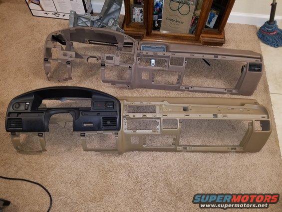 Two car dashboards laid out on a carpeted floor. One is black, the other is tan
