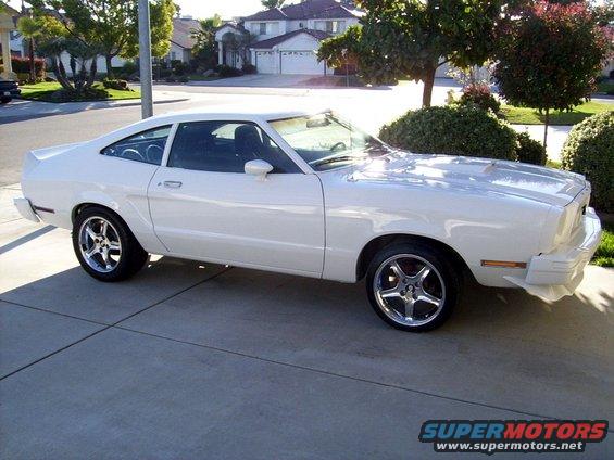 White coupe parked on a driveway. It has aftermarket wheels and a slightly modified front bumper
