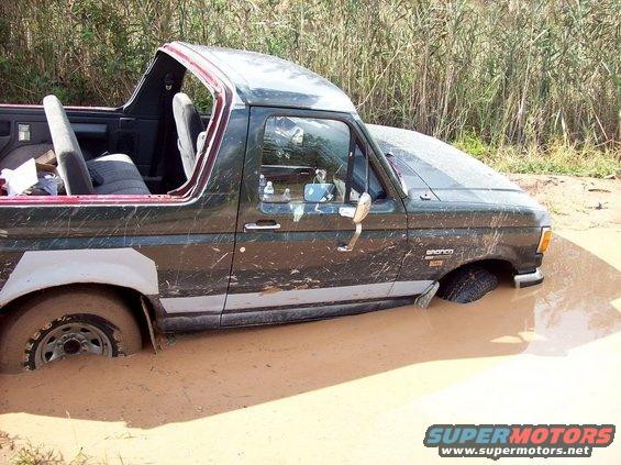Dark green Ford Bronco stuck in mud, driver's side visible, top removed