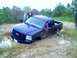 1989 Ford Bronco - A blue pickup truck is stuck deep in mud with two people nearby.