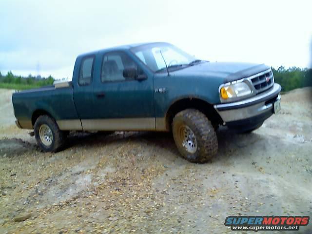 Green Ford F-150 pickup truck with tan lower body trim, lifted suspension, and off-road tires on a dirt mound