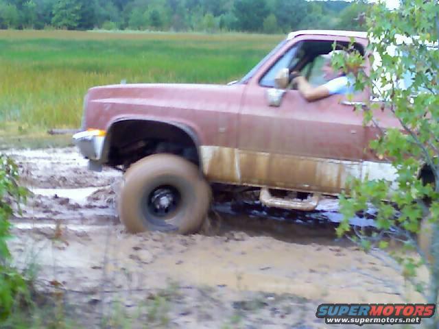Side view of a red pickup truck stuck in mud, with a driver visible