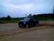 1989 Ford Bronco - A dark blue pickup truck drives on a dirt road, kicking up dust under a cloudy sky.