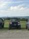 1989 Ford Bronco - Three lifted off-road vehicles are parked in a field under a cloudy sky.