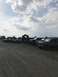 1989 Ford Bronco - Several SUVs and trucks are parked in a line on a gravel lot under a cloudy sky.
