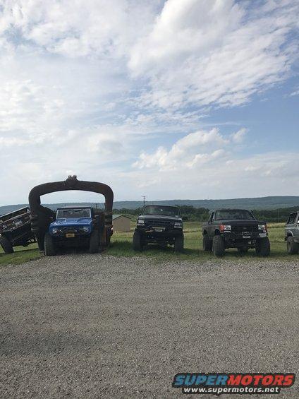 Blue Bronco and two black trucks parked outside