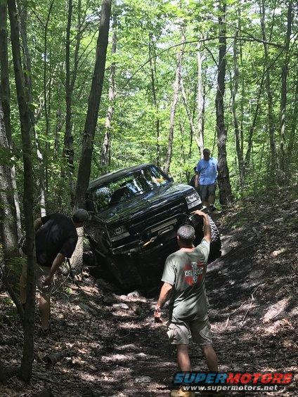 Black 1989 Ford Bronco navigating a steep, muddy trail with people watching