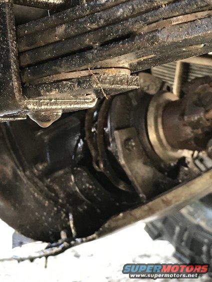 Close-up of a vehicle's leaf spring and axle assembly, showing a drip of fluid