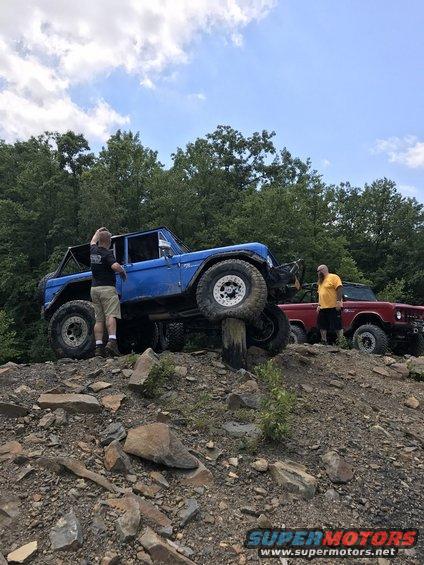 Blue 1978 Ford Bronco on rocky terrain with a person standing by the driver's door