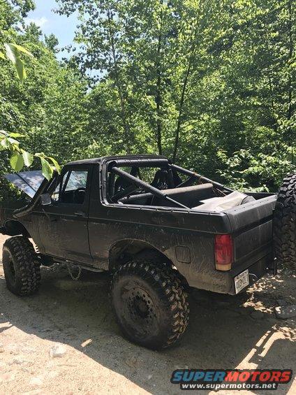Black Ford Bronco with roll cage, lifted suspension, and large tires parked on a dirt road