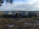 1989 Ford Bronco - A group of friends and their trucks pose for a photo in a grassy, open field under a cloudy sky.