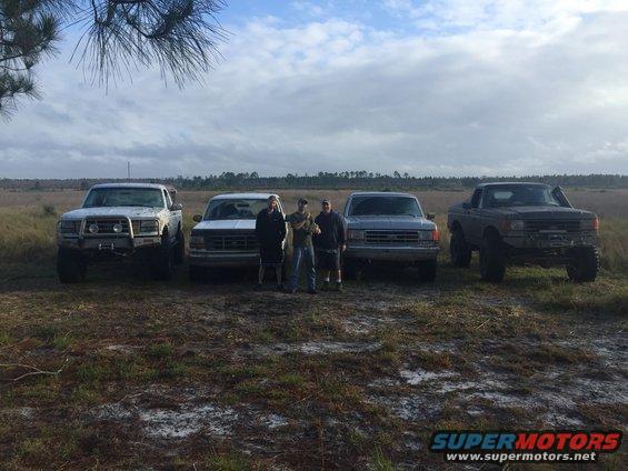 Four lifted trucks parked in a field with three men standing in front of them