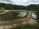 1989 Ford Bronco - Several vehicles navigate a challenging off-road course with muddy tracks and a body of water.