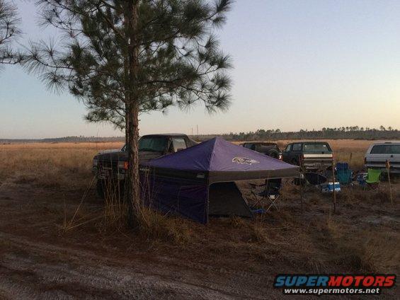 Campsite scene with a pop-up tent, chairs, and multiple SUVs parked in a field