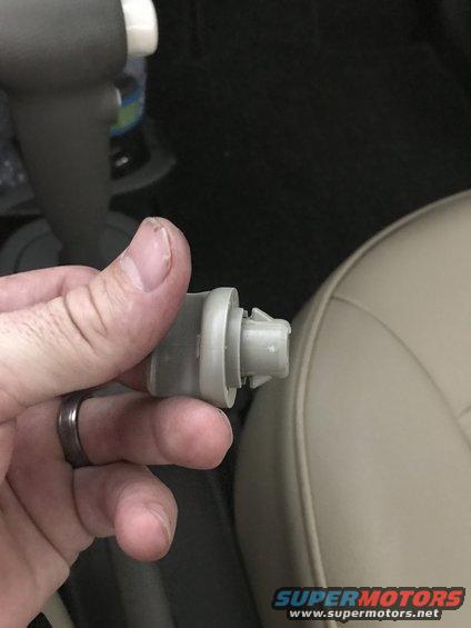 Hand holding a gray plastic clip, likely a fastener or trim piece