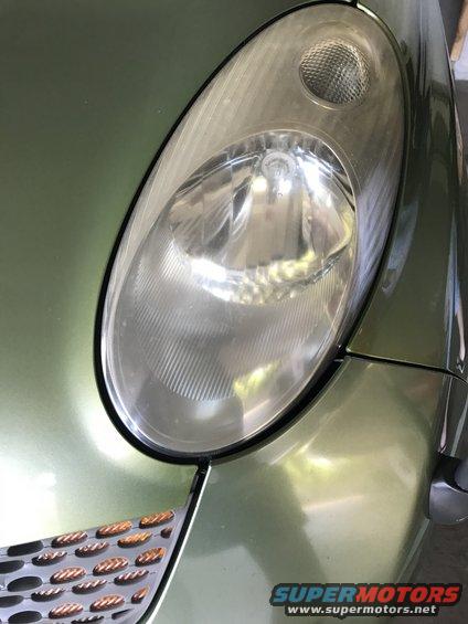 Close-up of a green car's headlight and part of the grille