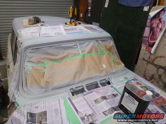 Car hood and windshield masked for painting, with paint can and tools on top