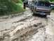 1989 Ford Bronco - Several vehicles navigate a challenging muddy trail, with one Bronco struggling to gain traction.