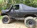 1989 Ford Bronco - A black 1989 Ford Bronco equipped with a snorkel and soft top navigates a muddy off-road trail.