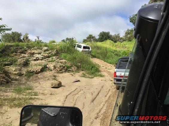 Silver and red SUV on a dirt road, with a white SUV ahead on a grassy hill