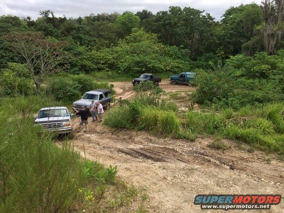 Silver pickup truck with people standing near it on a muddy dirt road
