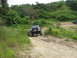 1989 Ford Bronco - A black SUV navigates a muddy dirt track surrounded by lush green vegetation.