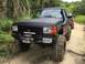 1989 Ford Bronco - Modified black Ford F-150 truck with off-road accessories parked on a dirt path.