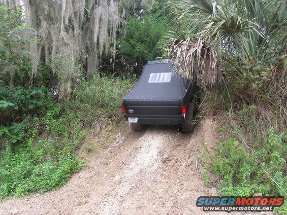 Black SUV with a soft top, angled on a muddy dirt path, surrounded by dense foliage