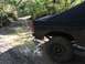 1989 Ford Bronco - A black SUV navigates a muddy path through a wooded area.