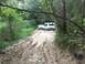 1989 Ford Bronco - A white SUV is stuck in a muddy trail surrounded by trees and foliage.