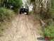 1989 Ford Bronco - A lifted truck navigates a steep, muddy incline surrounded by dense vegetation.