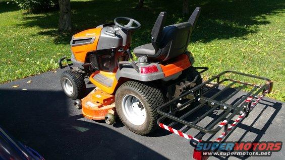 Orange and gray riding lawn mower with a black cargo carrier attached to the rear