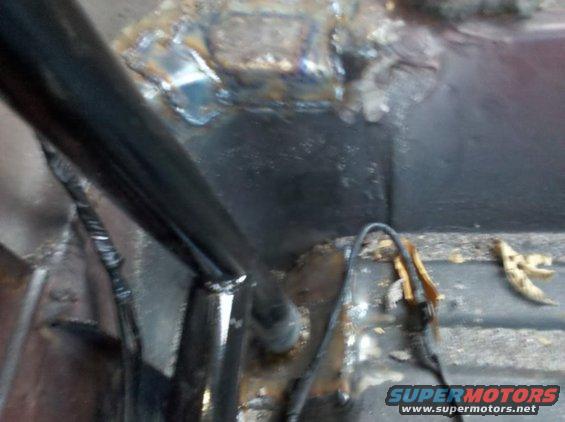 Vehicle interior floor with rust and welding marks. A black tube and wires are visible