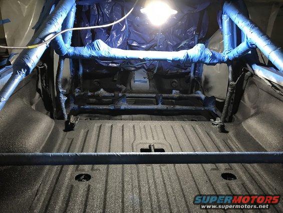Truck bed interior with roll cage and blue protective wrap, under a light