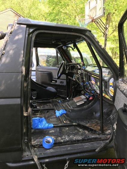Black 1989 Ford Bronco interior with removed seats, exposed wiring, and blue tape on the floor