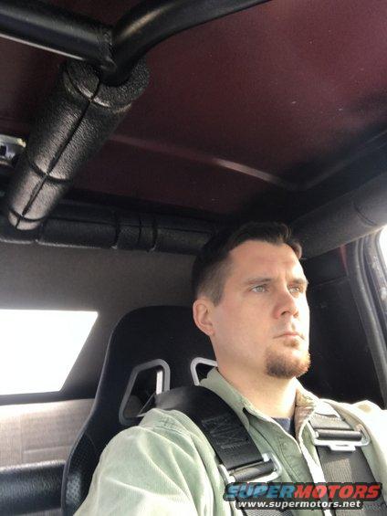 Man wearing a racing harness in a vehicle interior with a roll cage visible overhead