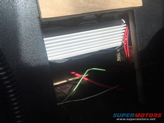 Car amplifier with fins and red and green wires visible inside a dark interior compartment