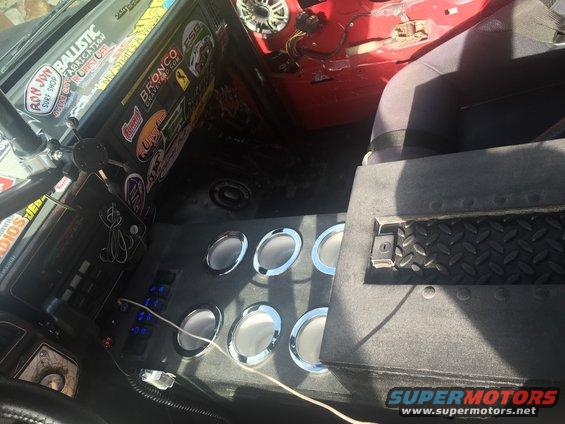 Interior shot of a vehicle with a custom console holding six speakers and multiple switches. The dashboard is covered in stickers, including one that says 'Bronco Graveyard.com'