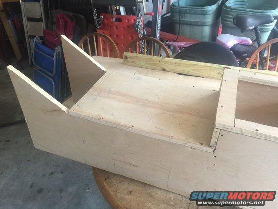 unfinished wooden box structure with angled front pieces, sitting on a round table