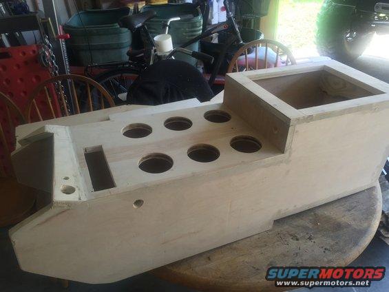 unfinished wooden console with multiple circular cutouts for cup holders, sitting on a table
