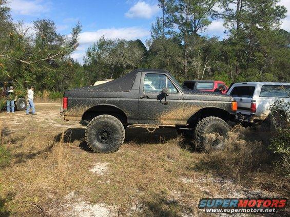 Black Ford Bronco covered in mud, lifted with large tires, seen from the side