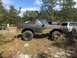 1989 Ford Bronco - A muddy black Ford Bronco is parked next to other vehicles in a wooded area.