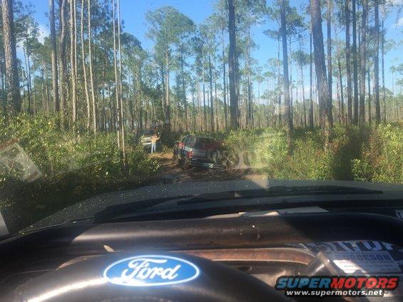 1989 Ford Bronco on a dirt road in a forest, with another vehicle behind it