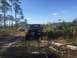 1989 Ford Bronco - Three SUVs, including a 1989 Ford Bronco, parked on a dirt path in a wooded area.